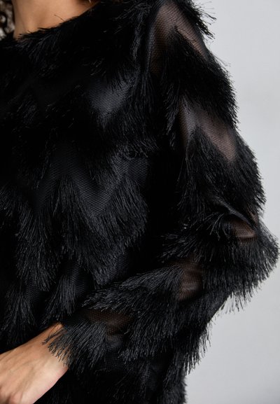 Μαύρη υφασμάτινη μπλούζα με κροσέ λεπτομέρειες σε ζιγκ-ζαγκ μοτίβο, με διάφανες ραφές στα μανίκια και στο λαιμό.