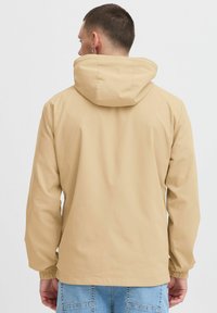 Beige hooded jacket with elastic cuffs, smooth texture, and a simple design. Visible stitching and a minimalist aesthetic.