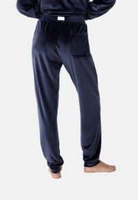 Pantalons de pyjama en velours bleu marine avec une taille élastique, une poche arrière unique et un design de jambe fuselée. Texture lisse, finition douce.