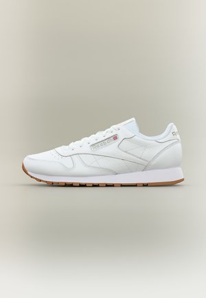 Бял нисък кожен кец Reebok класика с гумена подметка и лого отстрани и на петата на неутрален фон.