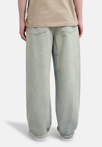 Ανοιχτό μπλε baggy τζιν με ξεθωριασμένη υφή, διακοσμημένο με δύο πίσω τσέπες και ίσια κοπή. Φορεμένο με απλό μπεζ τοπ.