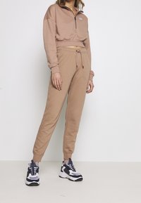 Beige kort sweatshirt med dragkedja och logotyp, kombinerad med matchande joggers med dragsko i midjan och texturerad tyg.