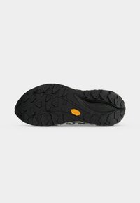 Semelle de chaussure noire robuste avec un motif de crampons profonds et un logo Vibram orange sur un fond clair uni.