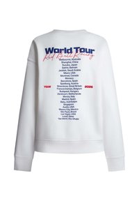 Άσπρη φόρμα με το κείμενο «World Tour Red Bull Racing» και μια λίστα με τους παγκόσμιους αγώνες του 2026 τυπωμένη στην πλάτη με μπλε και κόκκινα γράμματα.