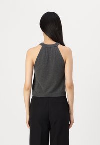 Grå ärmlös topp med hög halsringning, som har en avslappnad passform och stickad textur, kompletterad av en ribbad nederkant och öppen ryggdesign.