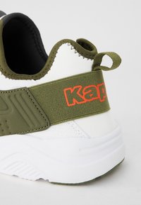 Vita sneakers med ett grönt elastiskt band med "Kappa"-logotyp i orange, texturerade detaljer och en vadderad sula med mönstrat grepp.
