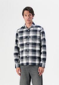 Marineblå og hvit rutete skjorte med lange ermer, knapper, brystlomme og løs passform. Stoffet virker mykt og middels tungt.