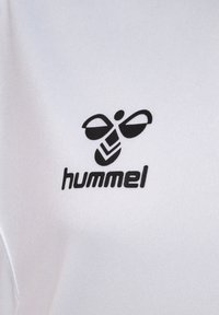 Tessuto bianco con logo Hummel nero, che include un'ape stilizzata e un design a chevron, con una texture liscia e una leggera lucentezza.