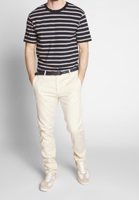Marineblå og creme stribet t-shirt med rund halsudskæring, creme bukser og brune sneakers. Har et sort bælte og en afslappet pasform.