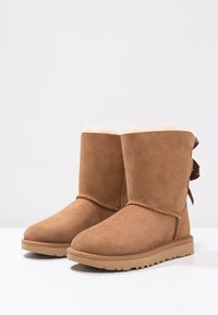 Bruine suede enkellaarsjes met een zachte, gevoerde voering van bont, een ronde neus, platte zool en een decoratieve strikdetail aan de achterkant.
