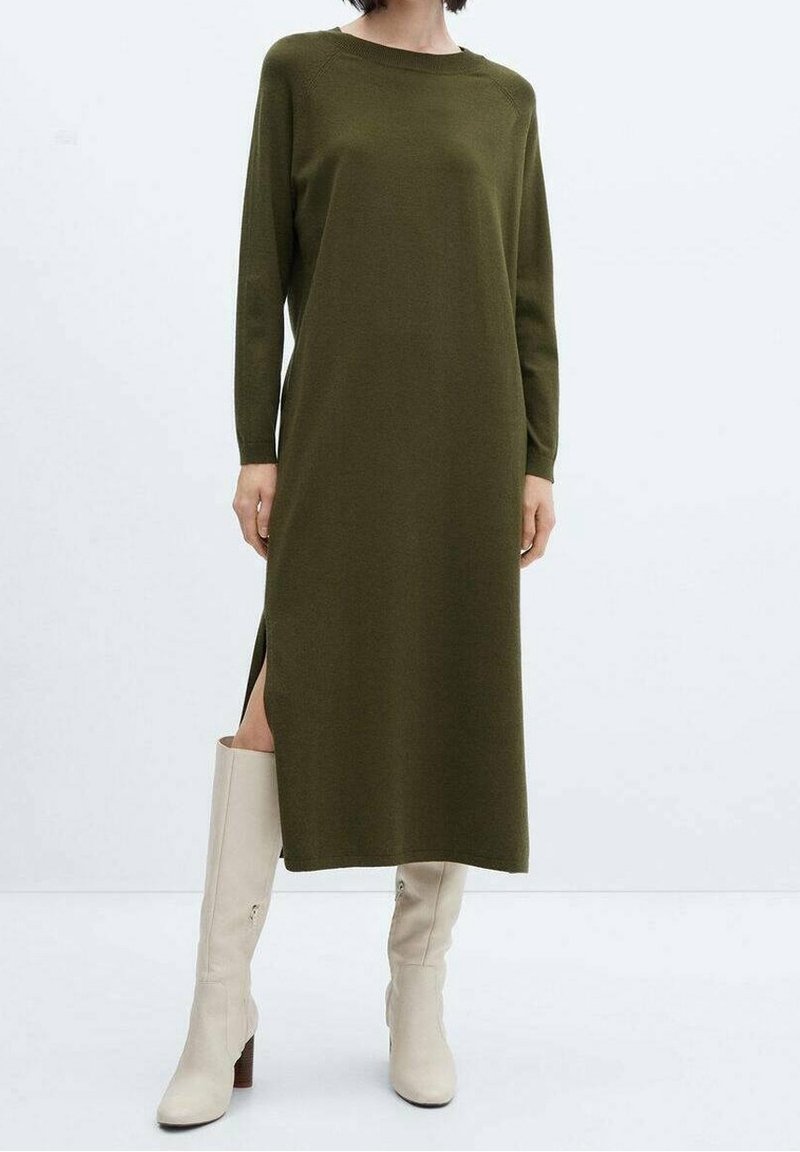 Femme portant une robe midi vert olive à manches longues avec fente latérale, assortie à des bottes beige hauteur genou sur fond uni.