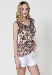 Top sans manches en rose pâle avec des motifs de feuilles marron foncé, encolure ronde et détails floraux. Associé à un short blanc.