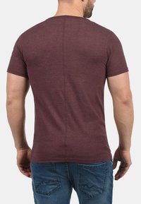 Burgunderfarget T-skjorte med korte ermer i et mykt, teksturert stoff med rett kant og bakseam, sammen med blå jeans.