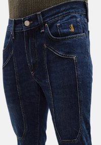 Jeans in denim blu scuro con un design slim fit, cuciture gialle a contrasto e un piccolo logo dettagliato sulla tasca anteriore.