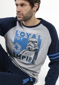 Conjunto de ropa de estar en casa en gris y azul marino que presenta un gráfico de un stormtrooper, el texto "Leal al Imperio" y rayas azules en las mangas y pantalones.