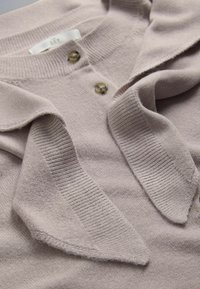 Soft beige knitted cardigan with ribbed collar and two brown buttons, shown folded with visible fabric texture.
