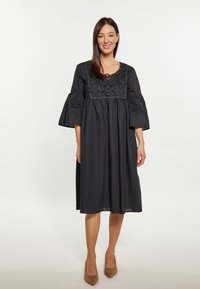 Rochie neagră din bumbac, cu mâneci tip clopot, guler brodat și croială lejeră. Până la genunchi, cu o textură fină și un design minimalist.