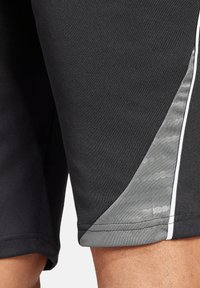 Schwarze Sportshorts mit einem grauen diagonalen Einsatz in glänzender Textur und weißen Akzentpipings entlang der Seitennaht.