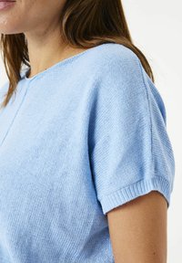 Hellblaues Stricktop mit kurzen Ärmeln, rundem Ausschnitt und einer subtilen Textur. Leicht lockere Passform mit gerippten Bündchen.