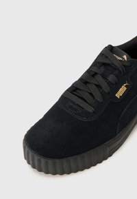 Black suede sneaker with textured surface, round toe, and thick rubber sole. Features black laces and a gold logo accent.