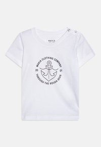 Camiseta blanca de manga corta hecha de algodón. Presenta un gráfico de ancla negra con texto circular. Dos botones de presión en el hombro para facilitar su uso.