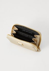 Portafoglio sintetico dorato con chiusura a zip, dotato di diversi scomparti per carte e un interno nero a motivo. Include un accento del logo in argento.