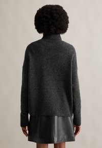Dunkelgrauer gestrickter Pullover mit hohem Kragen und fallenden Schultern, kombiniert mit einem schwarzen Lederrock. Weicher Stoff, lässiges Design.