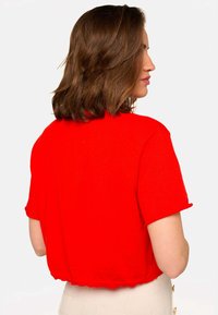 Haut court rouge à manches courtes fabriqué en tissu doux, avec un ourlet festonné et un design simple, adapté à un usage décontracté.