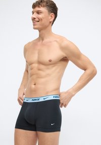 Czarne bokserki Nike mają jasnoniebieski pas z logo marki. Materiał wydaje się miękki i dopasowany, o gładkiej teksturze.