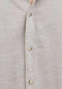 Camisa de botones gris claro hecha de tejido texturizado, con un pliegue frontal con botones perlados y un diseño sin cuello.