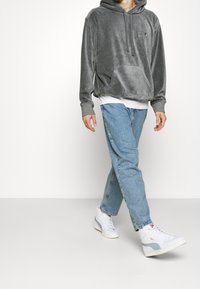 Sudadera con capucha de terciopelo gris y bolsillo frontal, combinada con jeans de mezclilla azul claro y zapatillas blancas con una franja azul claro.