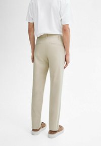 Beige trousers made of smooth fabric, featuring a tailored fit, straight legs, and two back pockets, paired with a white T-shirt and brown sneakers.