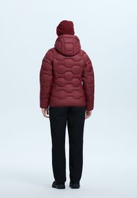 Burgundowa kurtka puchowa z sześciokątnym pikowaniem i kapturem, noszona z czarnymi spodniami i ciemnymi butami. Widok z tyłu, bezszwowy design.
