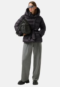 Sort pufferjakke med indsnøret talje og stor hætte, parret med lysegrå brede bukser og chunky sorte sko. Accessories inkluderer en skinnende sort taske og mørke solbriller.