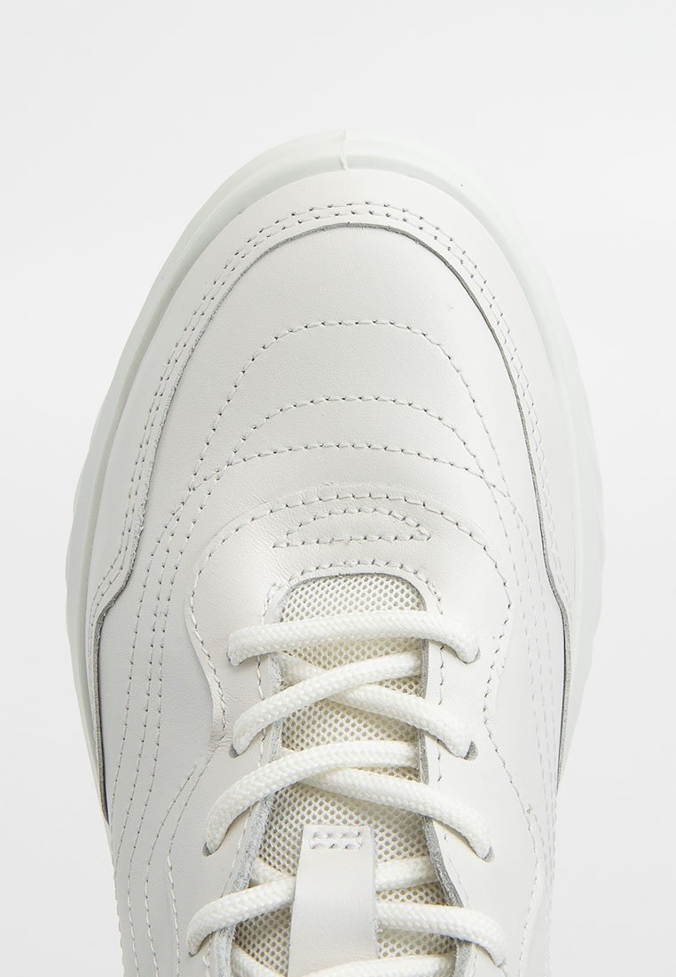 Zapatilla deportiva blanca con paneles de cuero texturizado, cordones blancos y lengüeta de malla, mostrada desde una vista superior.