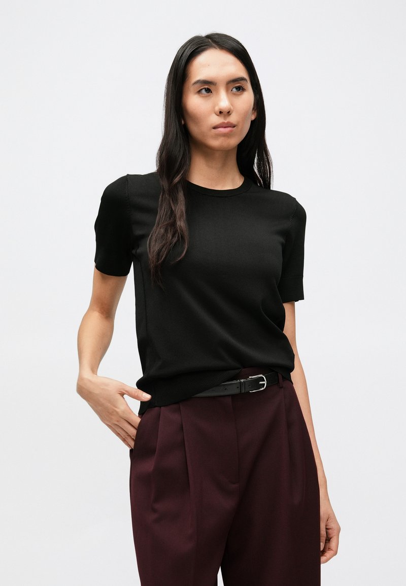 Black short-sleeve knit top with a round neckline, smooth texture, fitted design, paired with high-waisted burgundy trousers and a black belt.