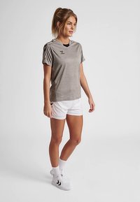 Szary sportowy T-shirt z krótkimi rękawami, z prążkowanymi akcentami na ramionach, w połączeniu z białymi szortami oraz czarno-białymi niskimi sportowymi butami.