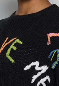 Černý pletený svetr s vícebarevnými vyšívanými vzory v oranžové, zelené, růžové a modré barvě. Má kulatý výstřih a texturovanou tkaninu.