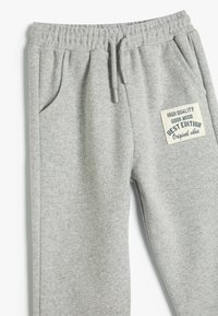 Grå sweatpants med ribbet tekstur, elastisk talje med snøre, sidelommer og et labelpatch med tekstdetaljer.