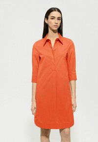 Kragenkleid in leuchtendem Orange, aus glattem Baumwollstoff. Mit Dreiviertelärmeln und einem lockeren Schnitt, der knapp über dem Knie endet.