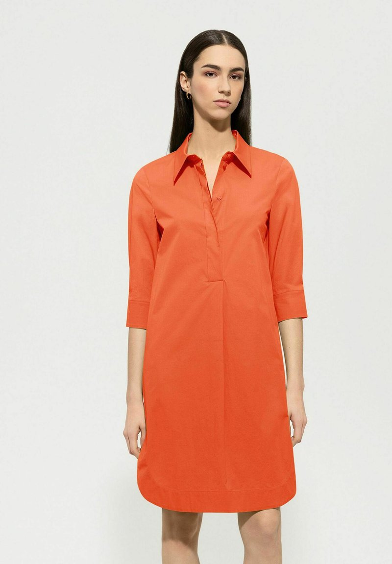 Kragenkleid in leuchtendem Orange, aus glattem Baumwollstoff. Mit Dreiviertelärmeln und einem lockeren Schnitt, der knapp über dem Knie endet.