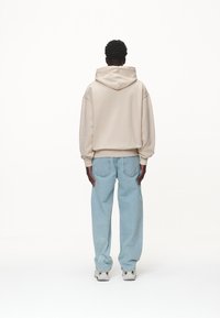 Sweatshirt beige à capuche au fit décontracté, associé à un pantalon en denim bleu clair. Texture lisse, poignets côtelés et détails de coutures visibles.