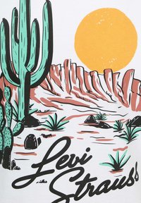 Camiseta blanca con un diseño gráfico que presenta cactus verdes, un sol amarillo y un terreno rocoso en tonos rosa y marrón, con el texto "Levi Strauss".