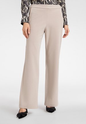 Beige wijde broek met een zachte textuur, uitgerust met een hoge taille. In combinatie met zwarte puntige schoenen versierd met strikken.