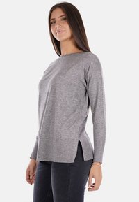 Maglione grigio a maniche lunghe con scollatura rotonda, orlo a coste, fessure laterali e una texture morbida, abbinato a jeans scuri.