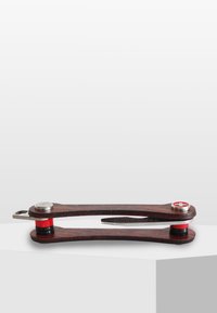 Trämultiverktyg med mörk finish, silverdetaljer, röda accenter och en böjd design. Bladet fälls ut från sidan för användning.