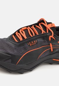 Mustmust ja hallid matkingujalad, millel on tekstuuriga pind, erksad oranžid paelad, Gore-Tex bränding ja rohkete haardetega tald.