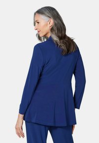 Marineblaues langärmliges Oberteil mit ausgestelltem Design, glatter Textur und dezenten Stichdetails entlang dem Saum und den Ärmeln.