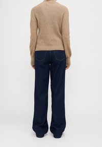 Maglione beige a coste abbinato a pantaloni in denim a gamba larga blu scuro. Il maglione presenta un collo alto e una silhouette aderente.