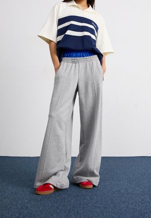 Lösa grå mjukisbyxor med elastisk midja, kombinerade med en marinblå och vitrandig pikétröja. Röda sneakers fullbordar outfiten.